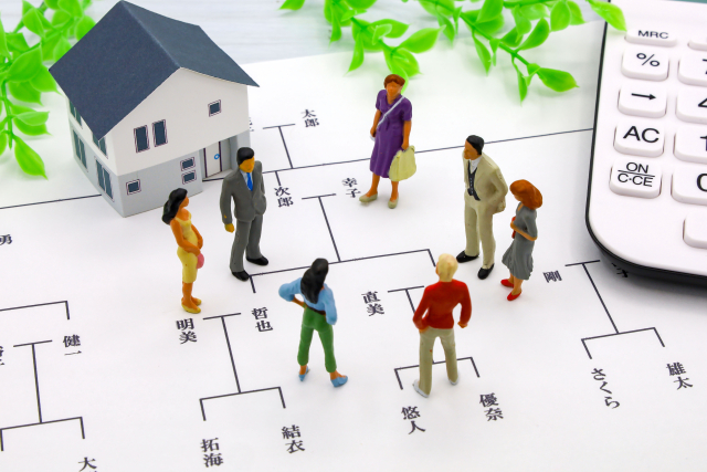 Miniature house with toy people gathered around a housing layout plan and a nearby calculator, suggesting real estate planning.